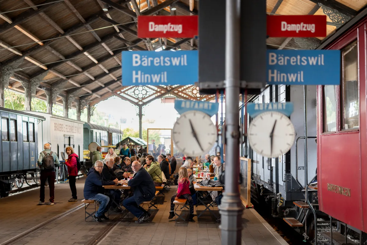 Während des «Stillstands» konnten sich die Anwesenden in der historischen Bahnhofshalle in Bauma stärken. Menschen sitzen an Tischen in einer alten Bahnhofshalle.